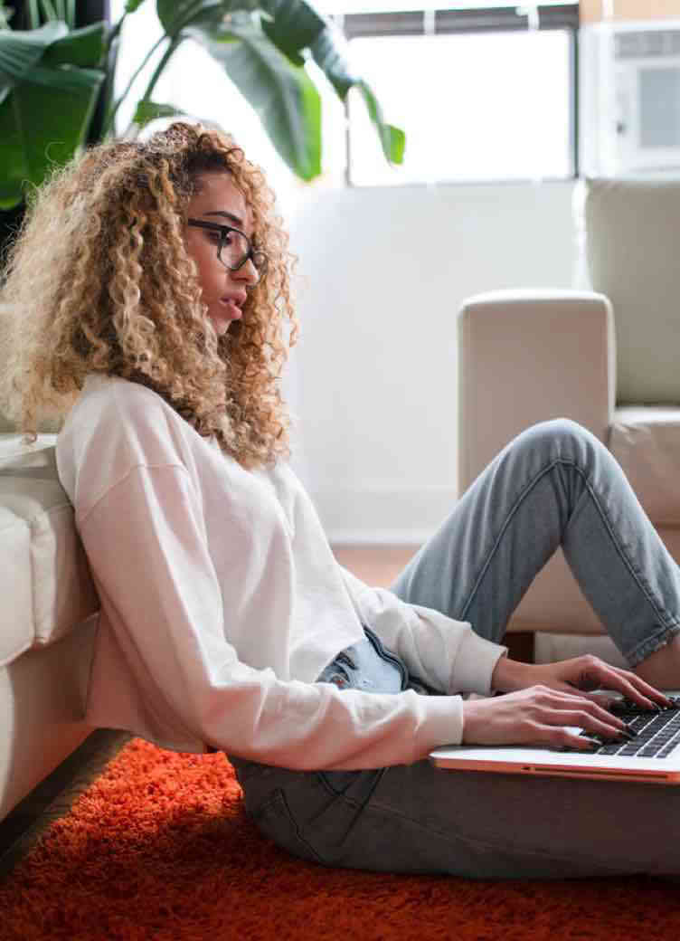 A woman sitting on the floor typing on her laptop